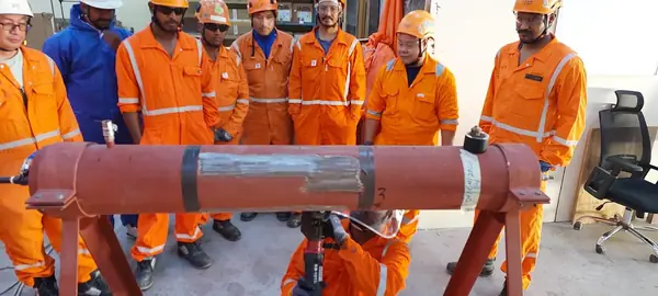 Crew in orange coveralls beside a red pipe section with a repair wrap applied