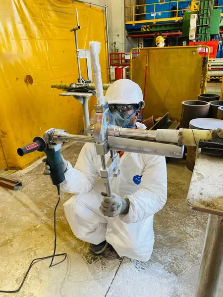 Technician using an angle grinder on a wrapped pipe test piece