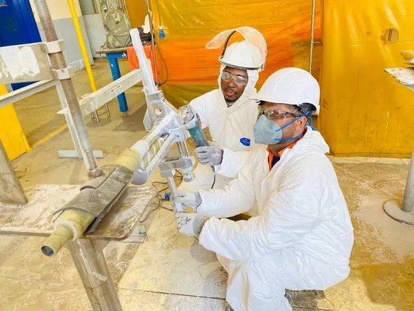 Technicians in protective suits working on a wrapped pipe test piece