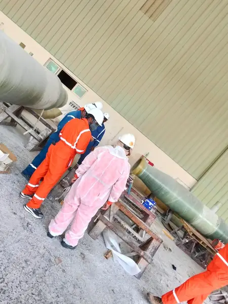 Crew in protective suits beside large green pipe sections in the workshop