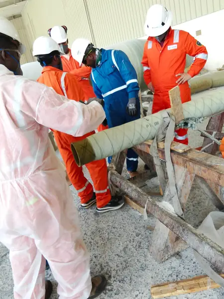 Crew handling a wrapped pipe section on trestles in the workshop