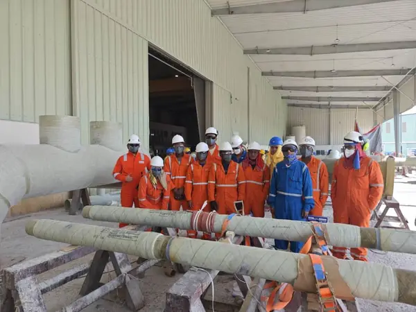 Crew with wrapped pipe sections on trestles in the workshop